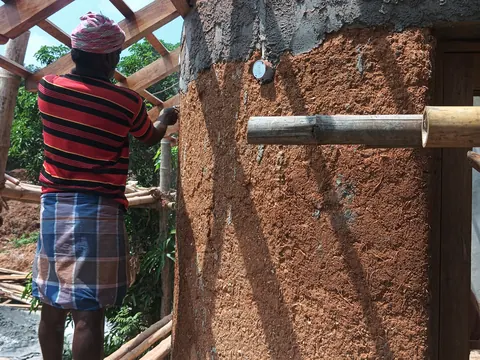 A builder pressing earth plaster onto a wall